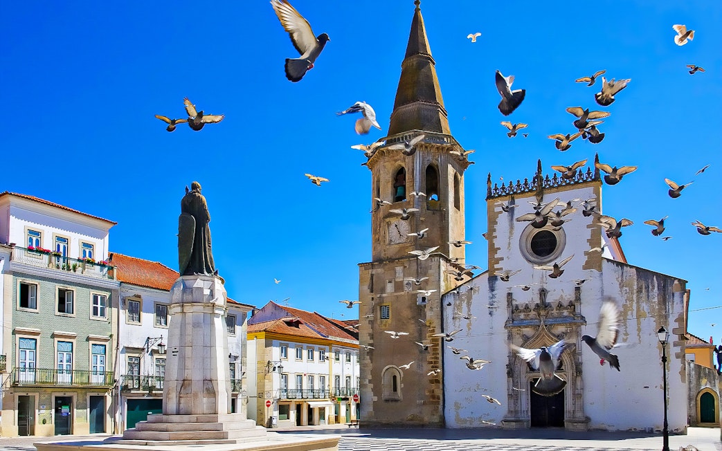 Historic church and statue in Tomar, Portugal, with pigeons flying, part of Knights Templar Tour from Lisbon.