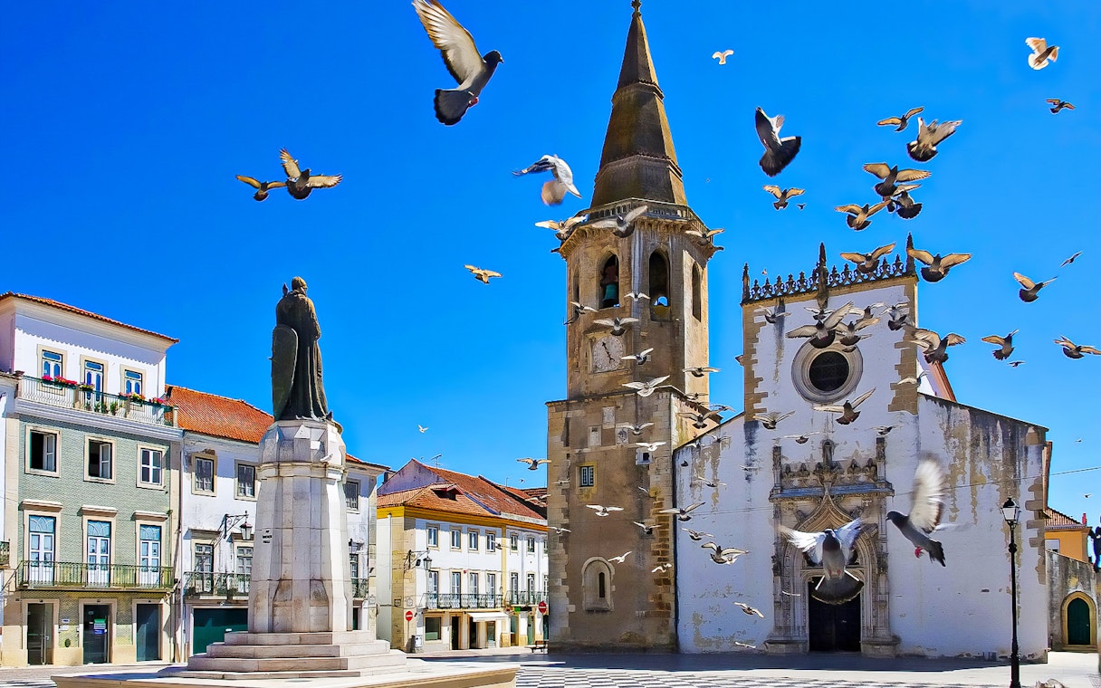 Historic church and statue in Tomar, Portugal, with pigeons flying, part of Knights Templar Tour from Lisbon.