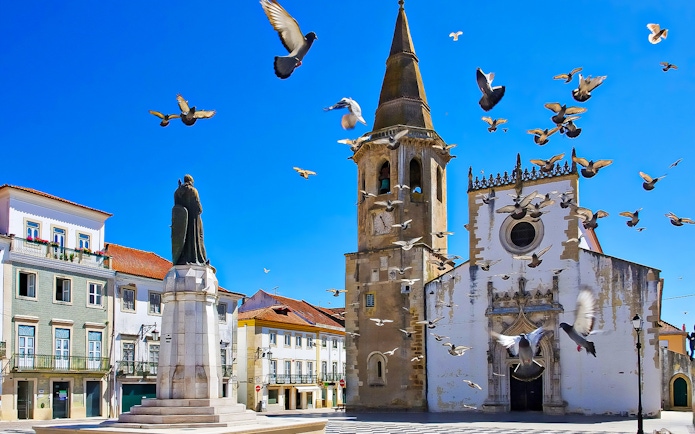 Historic church and statue in Tomar, Portugal, with pigeons flying, part of Knights Templar Tour from Lisbon.