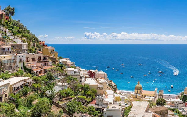 Positano coastline with colorful hillside buildings and boats on the blue sea, Italy.
