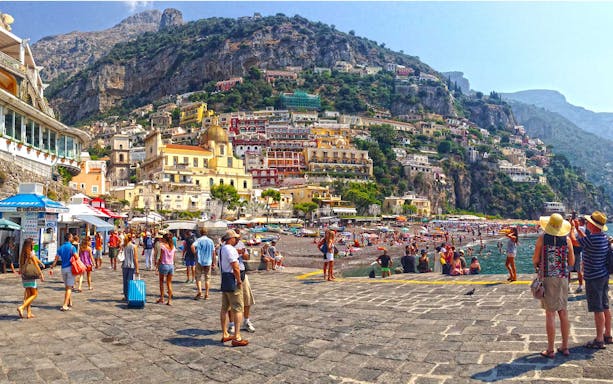Tourists exploring Positano beach with colorful hillside buildings on Amalfi Coast.