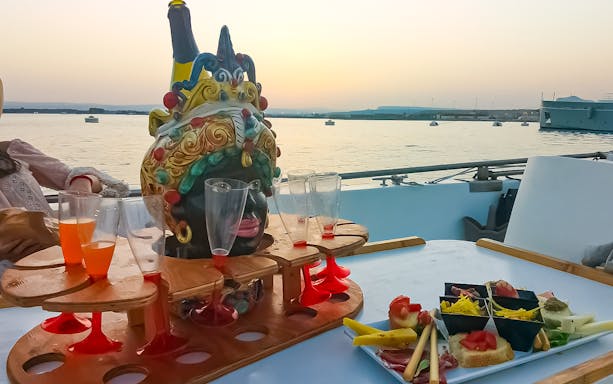 Sunset view from boat with aperitif and snacks on table, Ortigia Island tour.