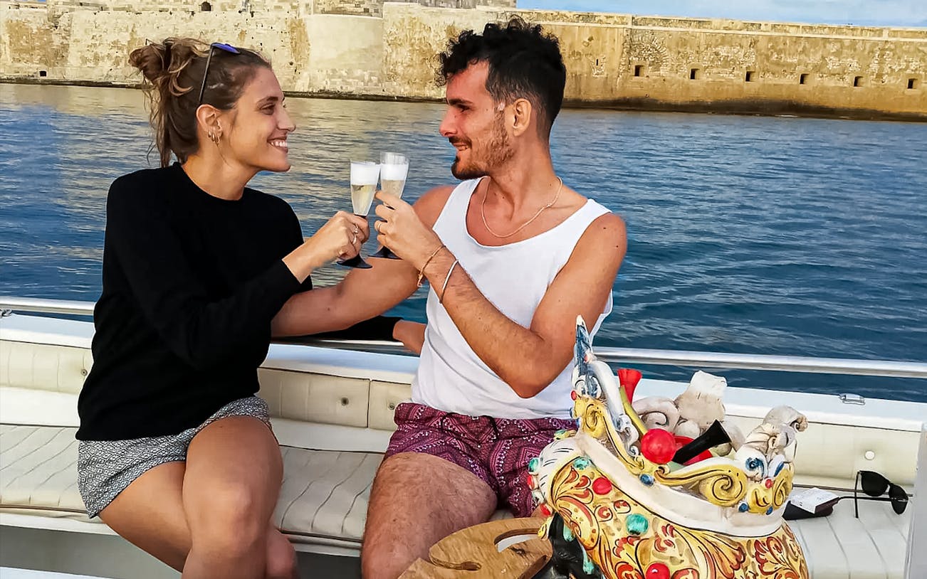 Couple enjoying aperitif on boat during sunset tour to Ortigia Island.