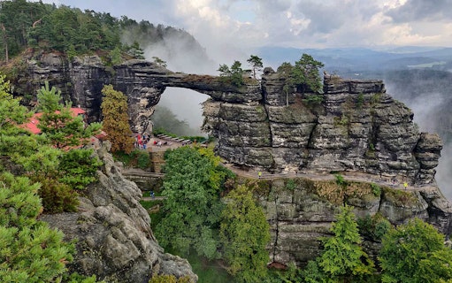 Pravčická Archway in Bohemian Switzerland National Park with misty forest backdrop.