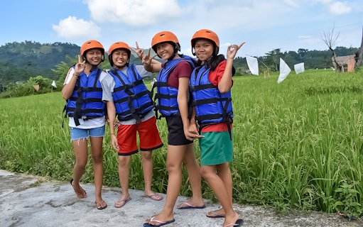 Group preparing for white water rafting on Telaga Waja River, wearing helmets and life vests.