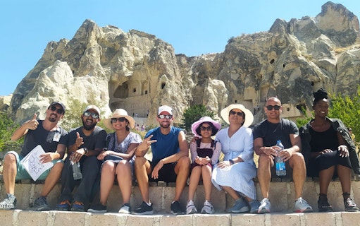 Group of tourists sitting in front of rock formations in Cappadocia during a guided tour.