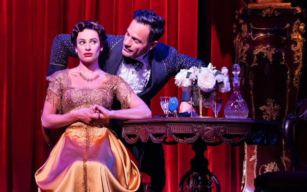 Actors performing a scene from "Funny Girl" on stage with red curtains.