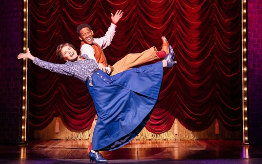 Performers dancing on stage in the musical "Funny Girl" with red curtain backdrop.