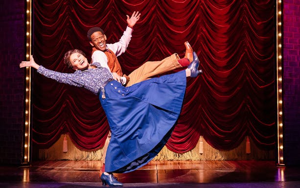 Performers dancing on stage in the musical "Funny Girl" with red curtain backdrop.