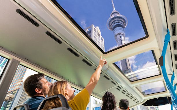 Passengers view Auckland Sky Tower through bus skylight on hop-on hop-off tour.