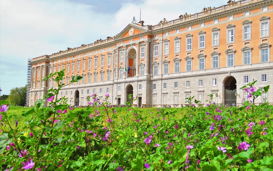 Royal Palace of Caserta facade with blooming flowers in foreground, Caserta, Italy.