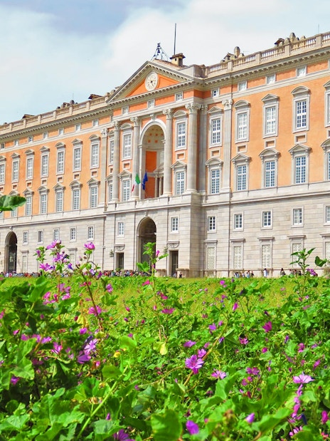Royal Palace of Caserta facade with blooming flowers in foreground, Caserta, Italy.