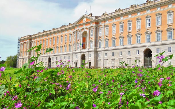 Royal Palace of Caserta facade with blooming flowers in foreground, Caserta, Italy.
