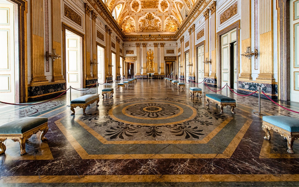Royal Palace of Caserta grand hall with ornate ceiling and marble floor.