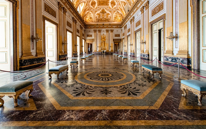 Royal Palace of Caserta grand hall with ornate ceiling and marble floor.