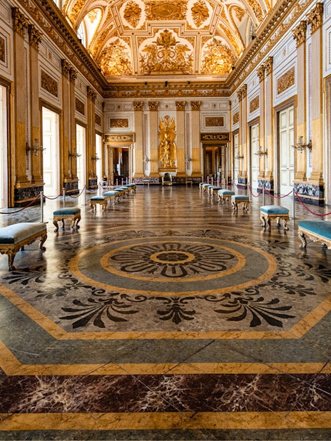 Royal Palace of Caserta grand hall with ornate ceiling and marble floor.
