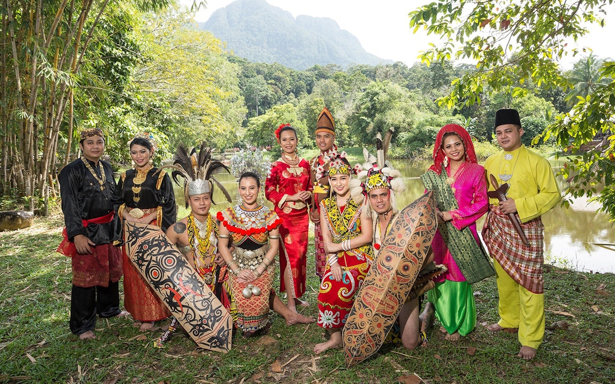 Traditional dancers in colorful attire at Sarawak Cultural Village, Malaysia, with lush greenery in the background.