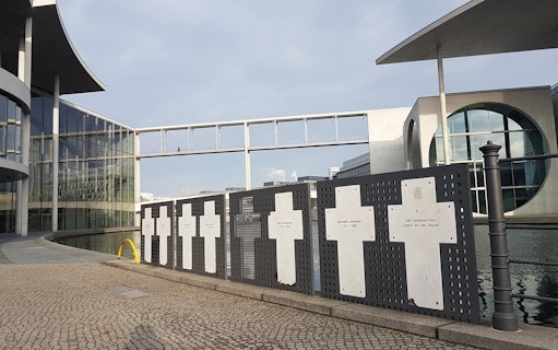 Memorial crosses at the Berlin Wall site near modern buildings and a footbridge.