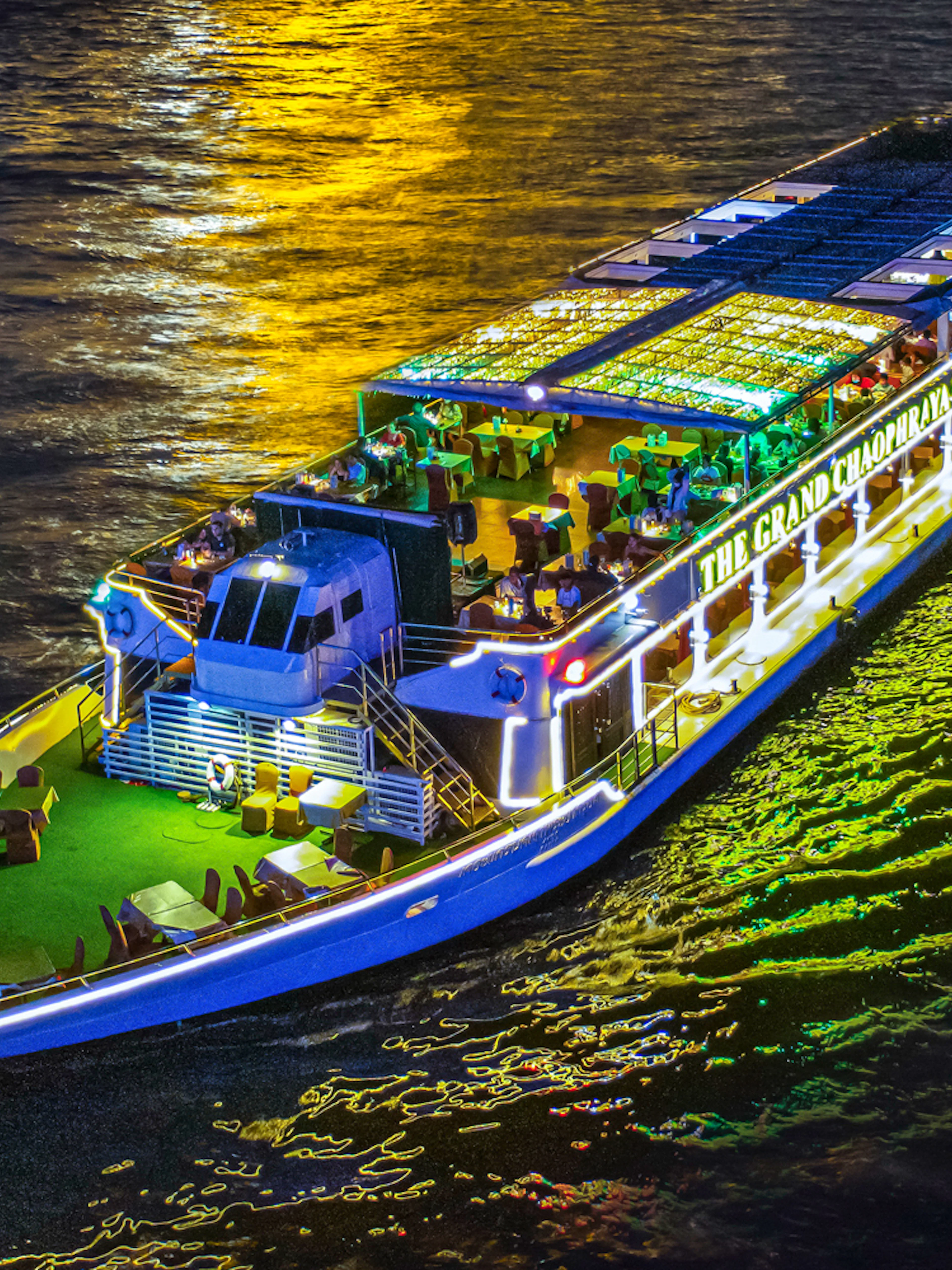 Chao Phraya river cruise ship illuminated at night with dining setup on deck.
