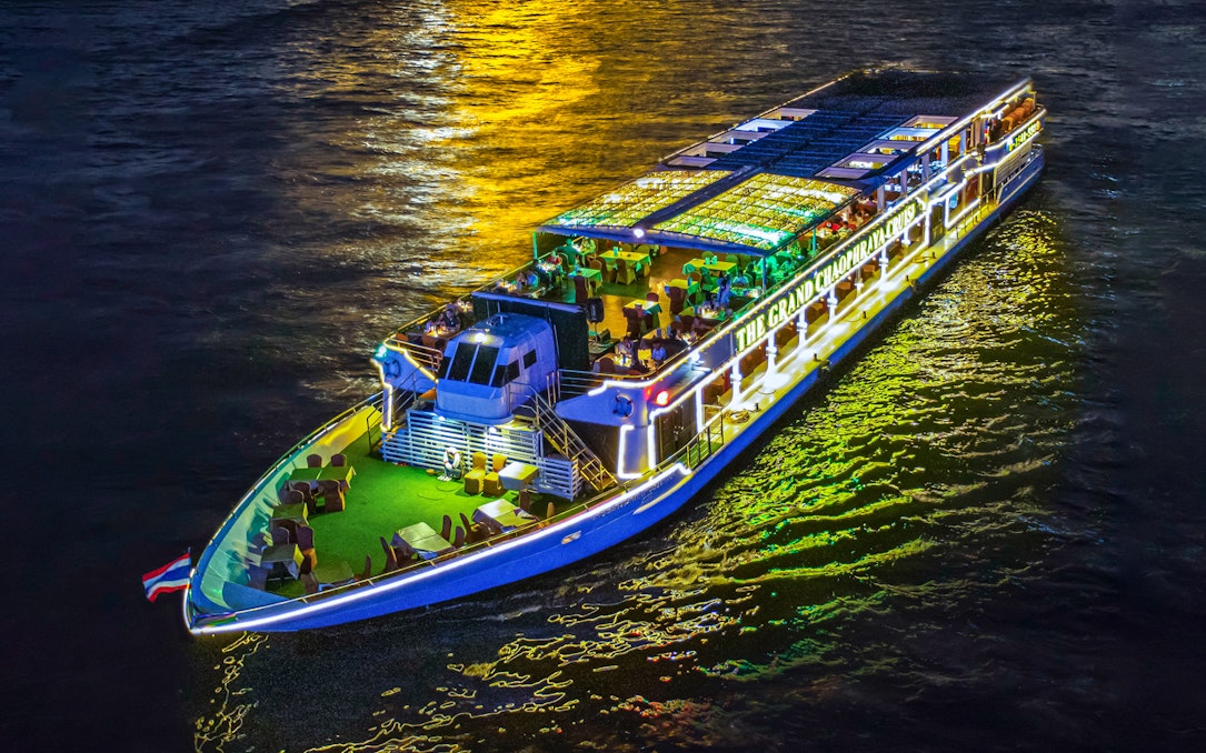 Chao Phraya river cruise ship illuminated at night with dining setup on deck.