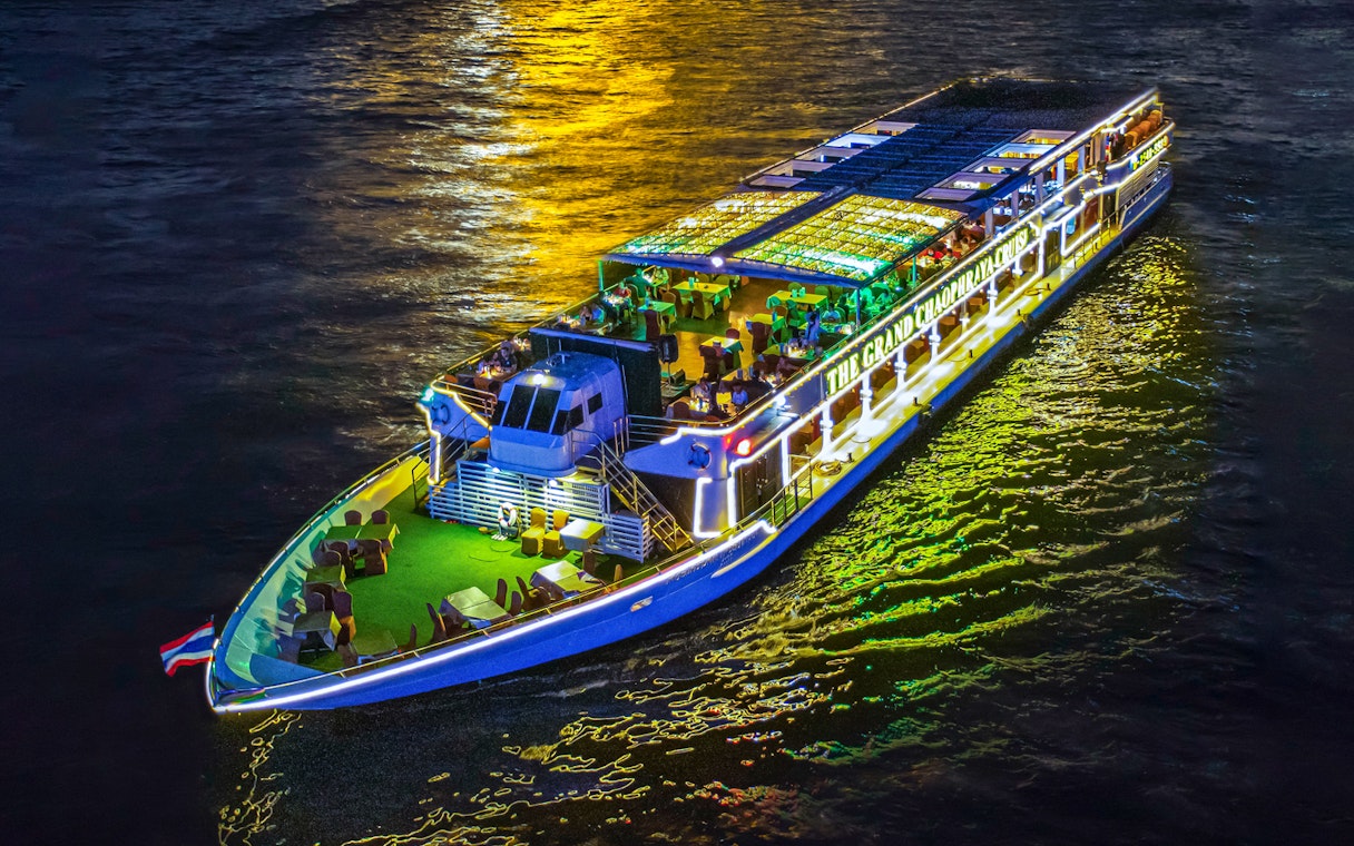 Chao Phraya river cruise ship illuminated at night with dining setup on deck.