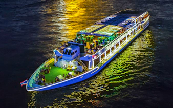 Chao Phraya river cruise ship illuminated at night with dining setup on deck.