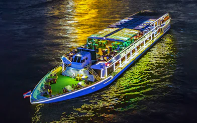Chao Phraya river cruise ship illuminated at night with dining setup on deck.
