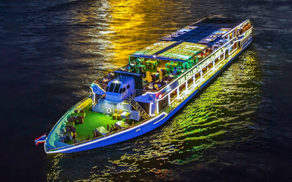 Chao Phraya river cruise ship illuminated at night with dining setup on deck.