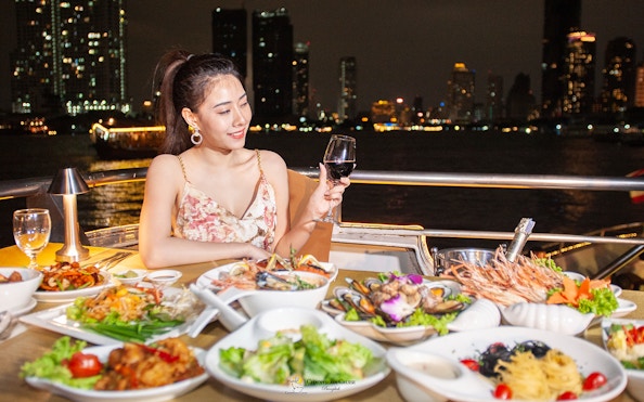 Buffet dinner on Chao Phraya Cruise with city skyline in Bangkok.