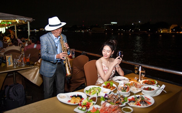 Saxophonist playing for a guest dining on the Chao Phraya Cruise in Bangkok.