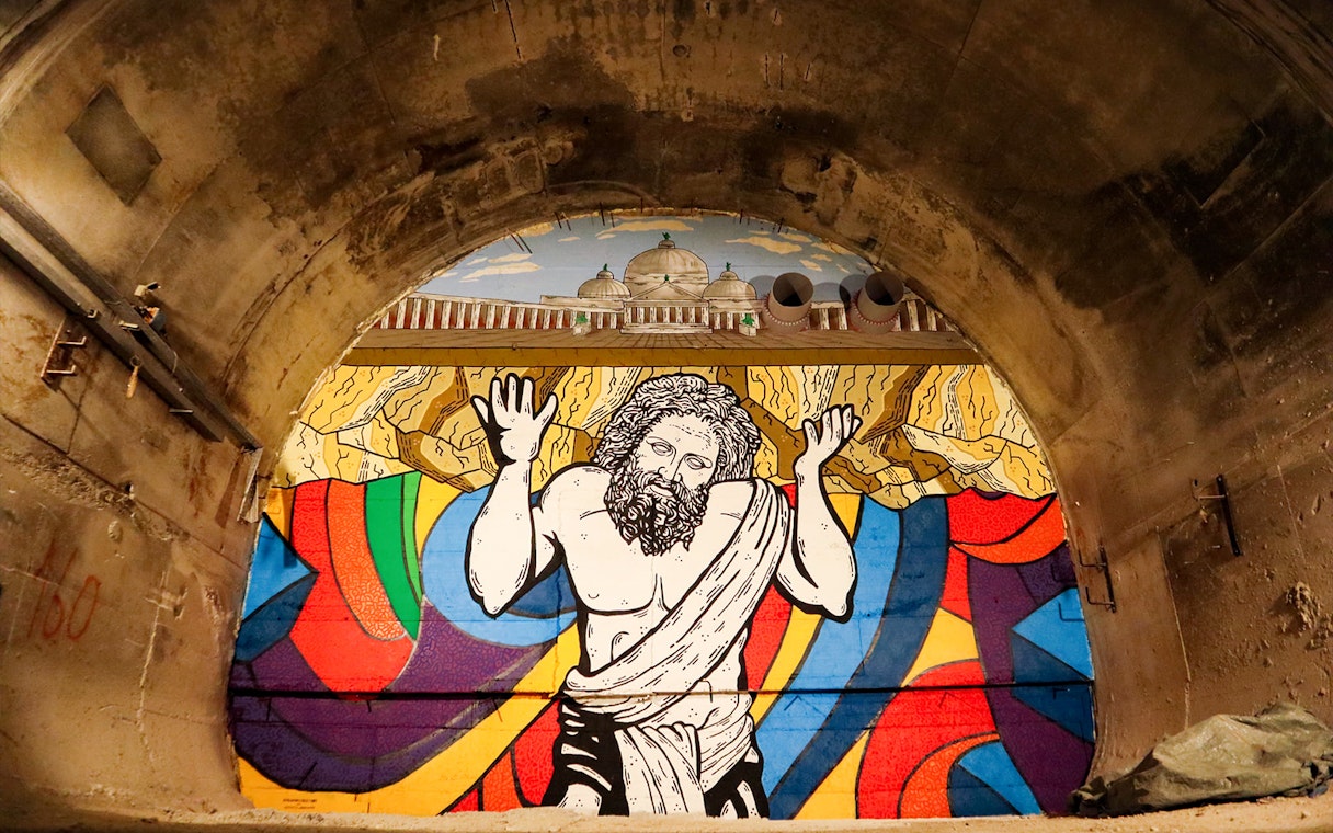 Mural of Atlas in Bourbon Tunnel, Naples, with colorful abstract background.