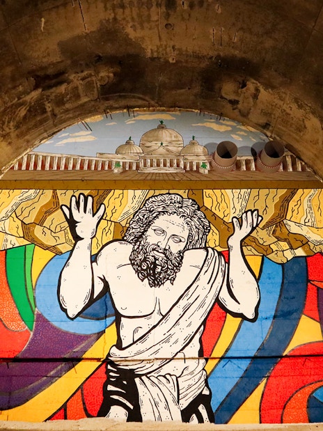 Mural of Atlas in Bourbon Tunnel, Naples, with colorful abstract background.
