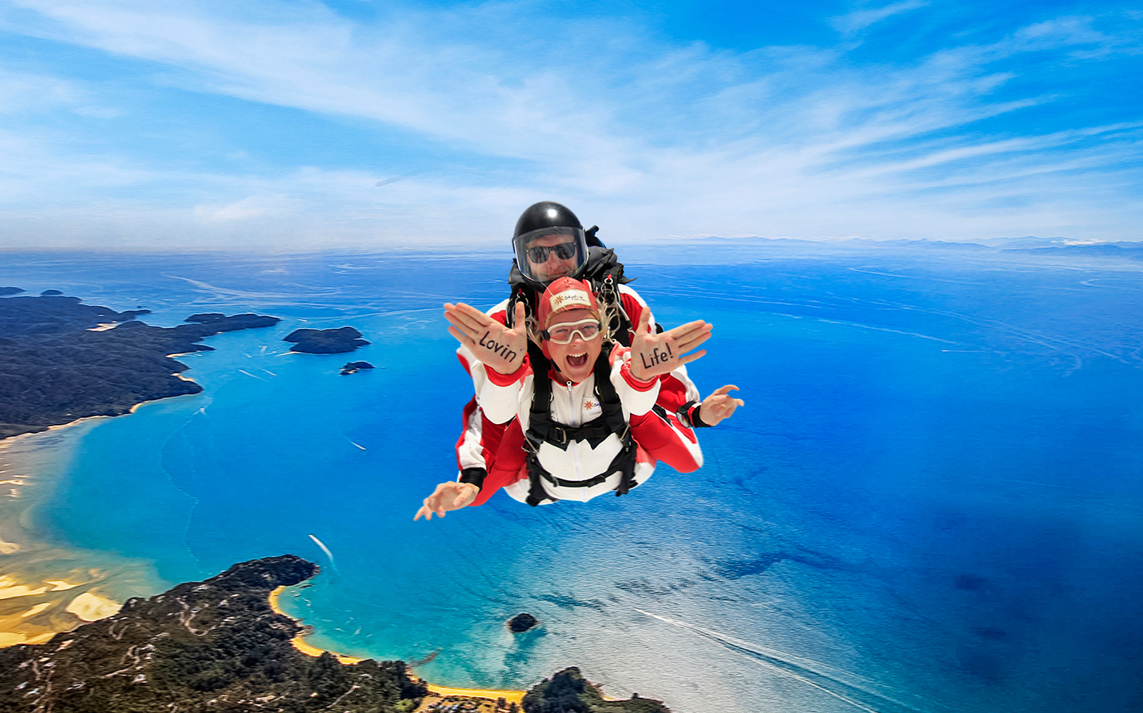 Skydivers over Abel Tasman National Park, New Zealand, with ocean and coastline below.