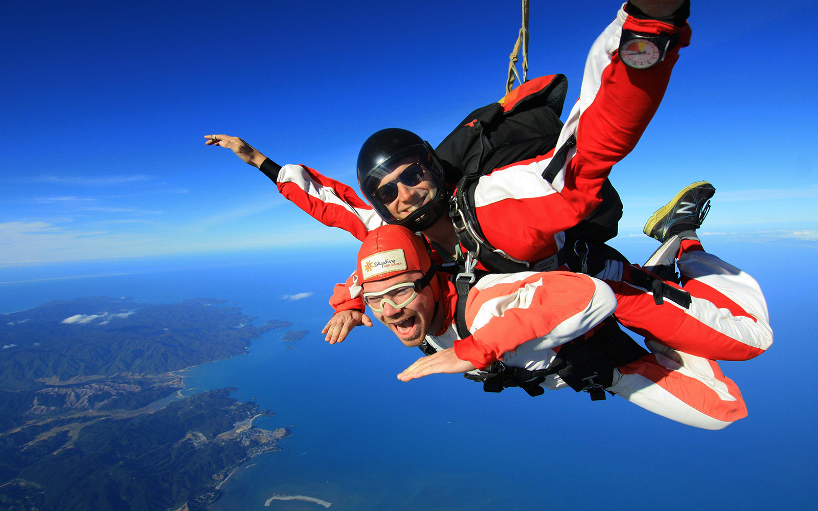 Skydivers tandem jumping over Abel Tasman, New Zealand, with ocean and coastline below.