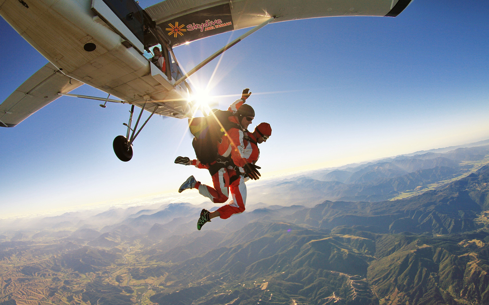 Skydivers jumping from plane over Abel Tasman, New Zealand, with mountains below.