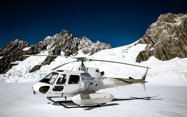 Helicopter on snowy alpine terrain with mountain backdrop, Ultimate Alpine Experience.