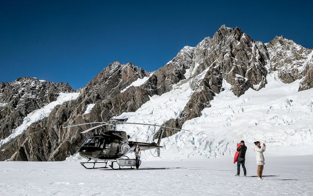 Helicopter on snowy alpine terrain with tourists capturing mountain views.