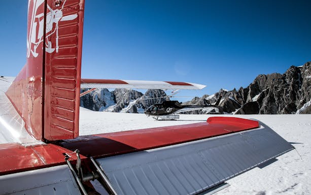 Helicopter and ski plane on snowy Southern Alps with mountain backdrop.