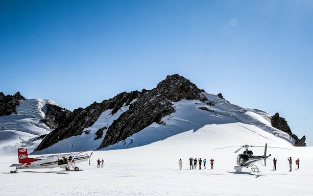 Helicopter and ski plane on snowy Southern Alps with tourists, New Zealand.