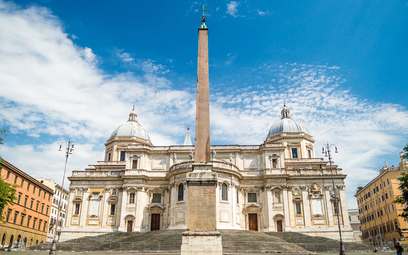 Santa Maria Maggiore Basilica with central obelisk in Rome under a blue sky.