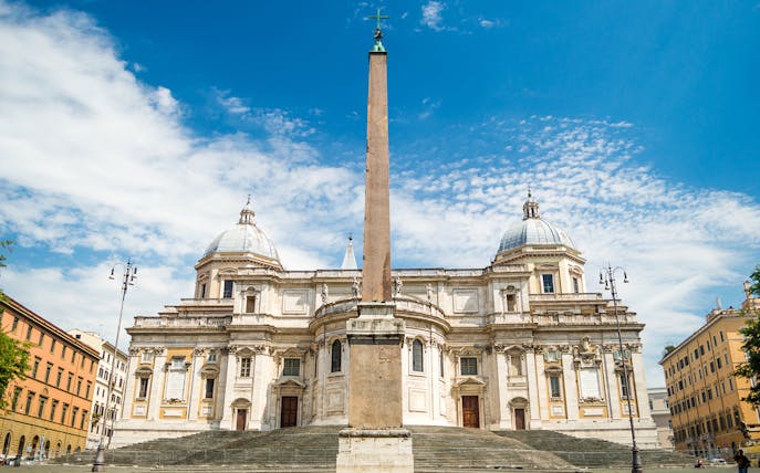 Santa Maria Maggiore Basilica with central obelisk in Rome under a blue sky.