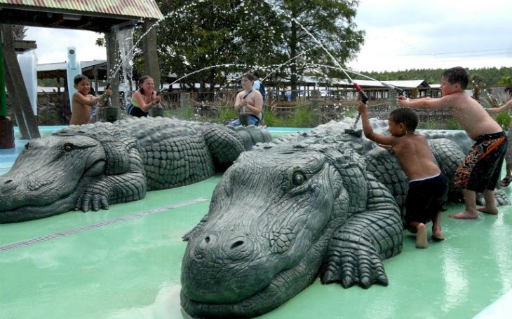 Children playing on alligator sculptures at Gatorland Park water area.