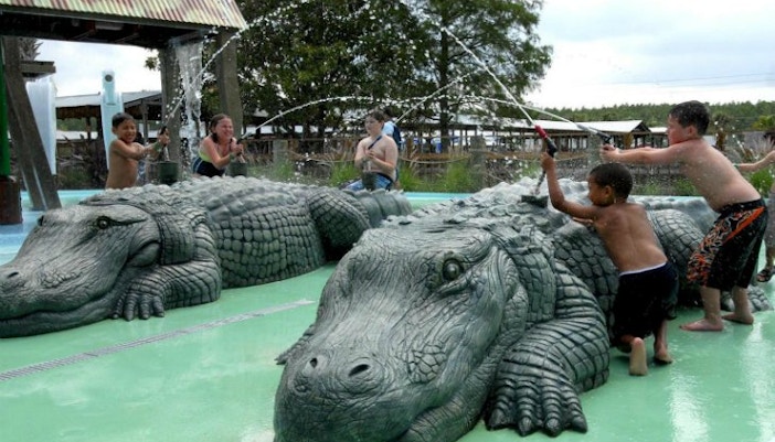 Children playing on alligator sculptures at Gatorland Park water area.