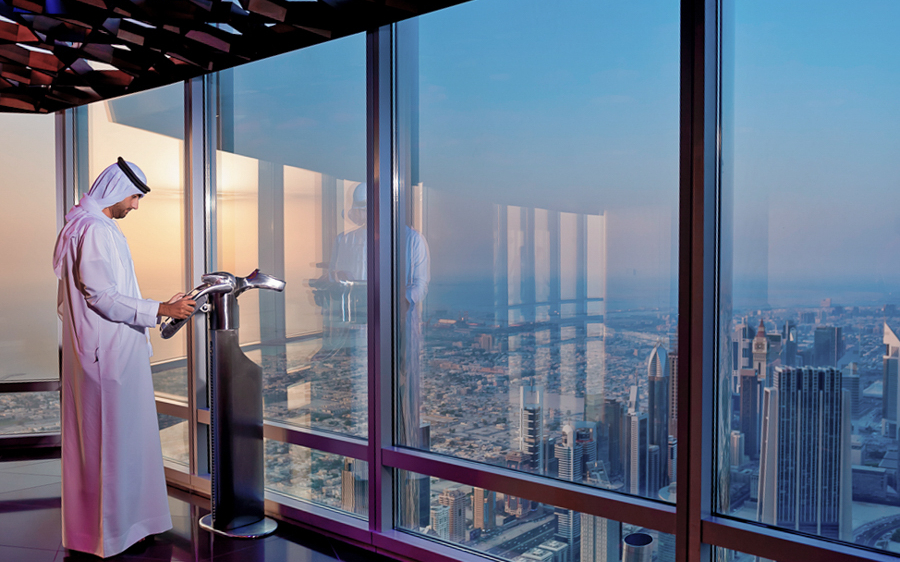 Man viewing Dubai skyline from Burj Khalifa's Level 124 at sunset.