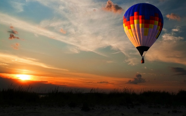 Hot air balloon floating at sunrise over a scenic landscape.
