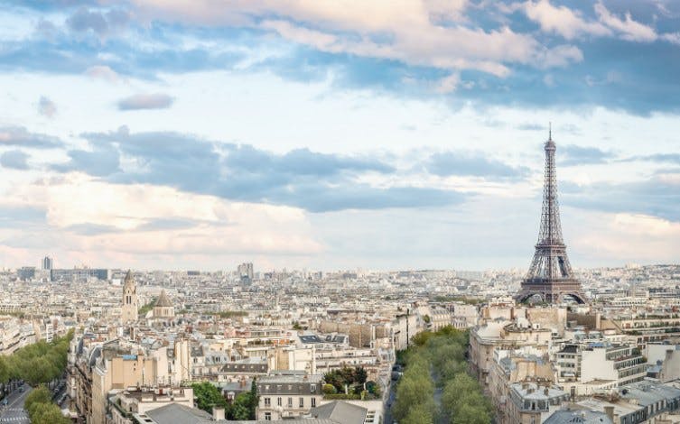 Eiffel Tower overlooking Paris cityscape under a cloudy sky.