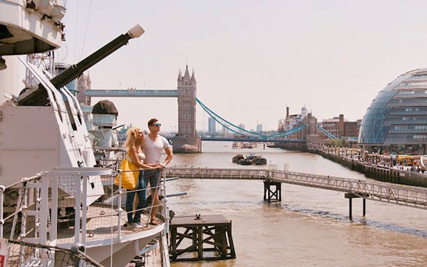 Couple on HMS Belfast deck with Tower Bridge in London background.