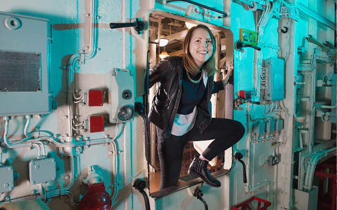 Visitor exploring interior of HMS Belfast through a hatch.