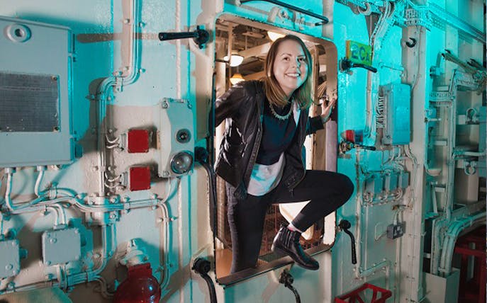 Visitor exploring interior of HMS Belfast through a hatch.