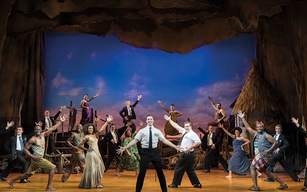 Cast performing a scene from The Book of Mormon musical on stage.